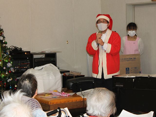 クリスマス会の風景 多目的室 クリスマス衣装のスタッフによる楽しいイベントが行われています。温かみのある空間で利用者の皆様が楽しんでいます。
