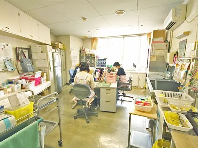 スタッフ作業室 内観   窓から光が入る明るい作業スペースです。机が並び、スタッフの方が落ち着いて作業しやすい様子が見られます。