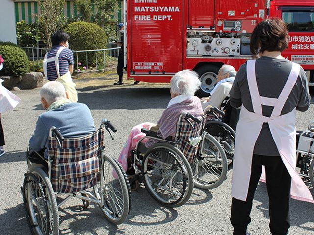 スタッフイメージ スタッフイメージ 車椅子の方々の近くで、介護スタッフがサポートしています。外での訓練の様子です。