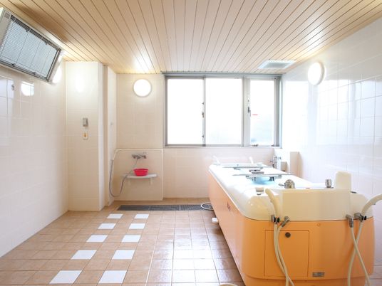 とても広い浴室で、介護用の特別な浴槽が設置されている。浴室内にはヒーターが設置されている。床のタイルがおしゃれな内装である。
