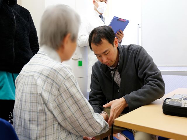 健康チェックを受ける様子 血圧測定 ケアスタッフが行う手厚いサポートをご覧いただけます。利用者とスタッフの丁寧なコミュニケーションが心地よい環境を作り出しています。
