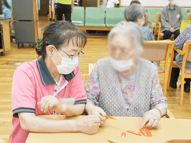 テーブルで活動中の人々 ラウンジ スタッフが利用者と一緒にテーブルで活動しています。交流を大切にした温かい空間です。