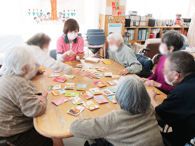 アクティビティ中の居室 居室 自然光がたっぷりと入る明るい居室で、入居者同士が楽しく交流しています。テーブル上のカードゲームも盛り上がっています。