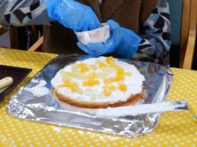 手作りケーキのデコレーション 料理 手袋をした手でケーキにフルーツを飾り付けており、手づくりの暖かさを感じる空間です。