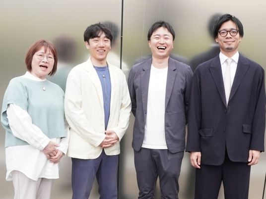 笑顔の4人が並ぶ外観前  