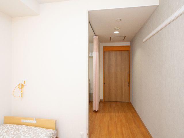 居室の照明とベッド 居室 広々とした個室は木目調のドアが特徴で、快適なプライベート空間を提供しています。自分の時間を大切に過ごしたい方に適しています。