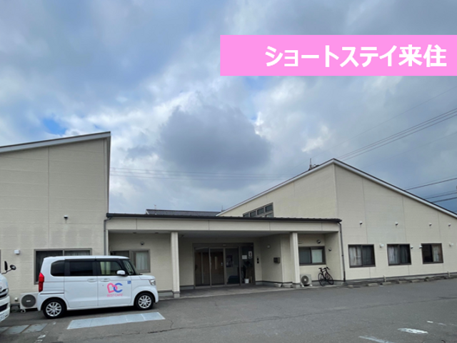 駐車場がある建物 外観 駐車場には車が停められており、施設の入り口も広々としています。青空が広がり、開放的な雰囲気です。