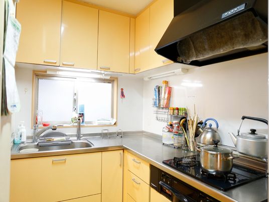 L字型にキッチンが敷設されており突き当たりがシンクになっている。右側にはコンロがあり鍋ややかんが置かれている。