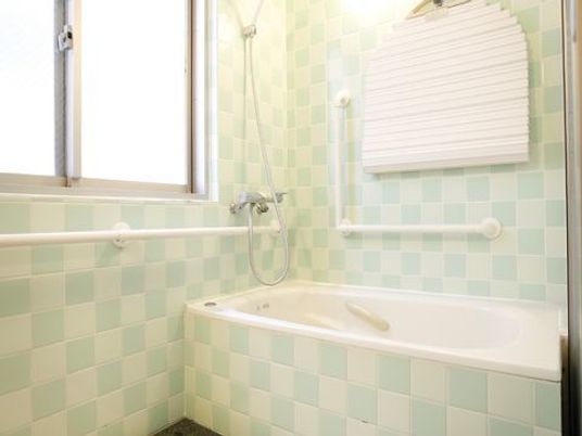 浴室内は白と薄いグリーンのタイルでできている。窓からは明るい光が差し込んでおり壁には手すりもついている。