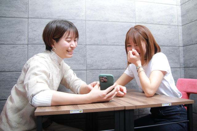 笑顔で携帯を見る二人 プロフェッショナルとして成長する機会も豊富に用意 明るく落ち着いた色の壁に囲まれた空間で、笑顔で携帯を見ながら楽しいひと時を過ごしている様子です。職員として、このような温かい瞬間をサポートするのも仕事の魅力の一つです。