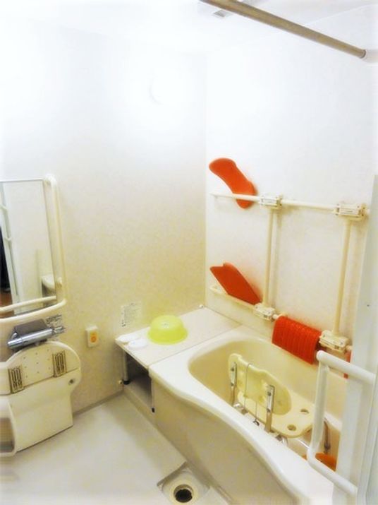 白い浴槽が置かれた広い浴室。シャワーや手すり、浴槽内にはシャワーチェアも設置されている。