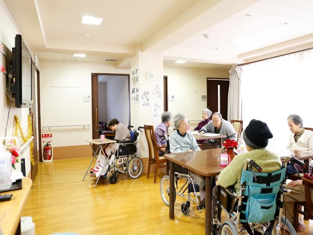 居住者のいる共有スペース リビング ゆったりとした食堂で利用者が食事や交流を楽しんでいます。明るく開放的な雰囲気の中で、皆様が笑顔で過ごされています。