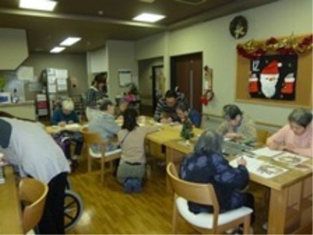共有スペースでの憩いの時間 レクリエーション ゆっくりと手工芸に興じる皆さんの姿が、温かい雰囲気の共有スペースを表しています。スタッフと利用者の交流も活発な環境です。