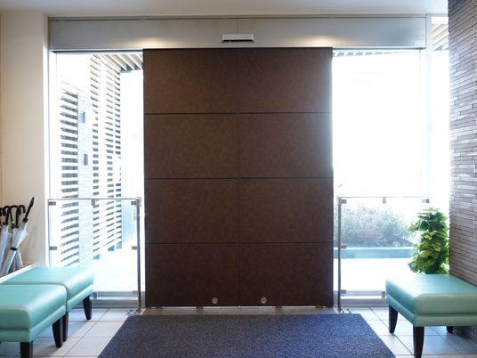 玄関の外へとつながる扉には、茶色い両開きの自動ドアが取りつけられている。両端には、椅子が3つ並べられている。