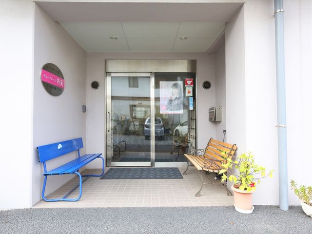快適な施設入口 玄関 清潔感のあるエントランスにはベンチが設置され、待ち時間も快適です。植物が彩りを添え、温かみのある歓迎空間となっています。