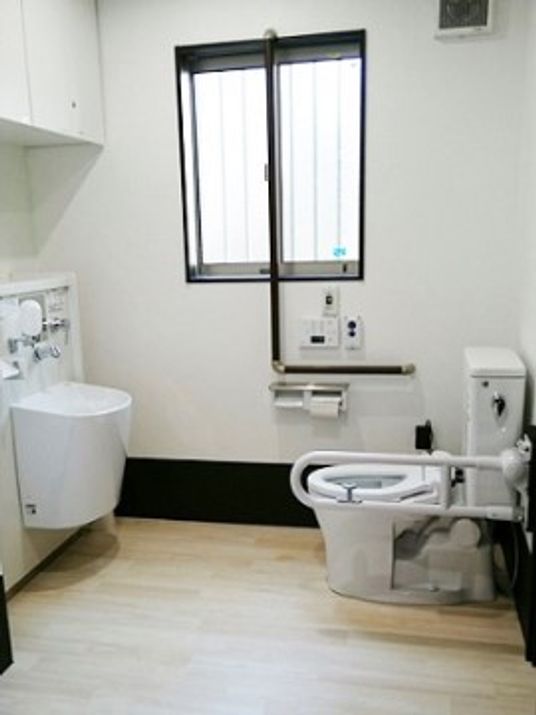 白を基調とした内装に、壁の下側と手すり、窓枠に黒を取り入れたトイレである。便座の正面に深さのある洗面台を設置している。