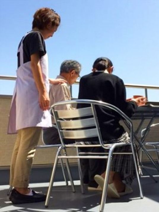 屋根のない屋外で、入居者様とスタッフがテーブルについて作業を行っている。外の空気に触れながらリラックスしてお過ごしいただける。