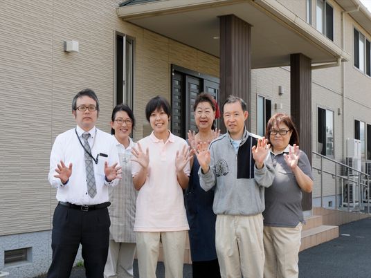 施設の玄関の前で撮影されたスタッフの写真である。６人それぞれが自由な服装をしており、仲良く映っている。