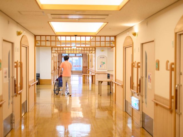 車椅子の人物がいる廊下 廊下 広々とした廊下で、車椅子の方も快適に移動しやすい環境です。スタッフがサポートしています。