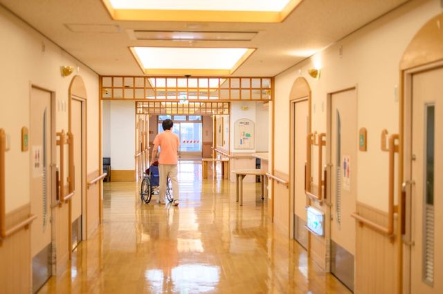 車椅子の人物がいる廊下 廊下 広々とした廊下で、車椅子の方も快適に移動しやすい環境です。スタッフがサポートしています。