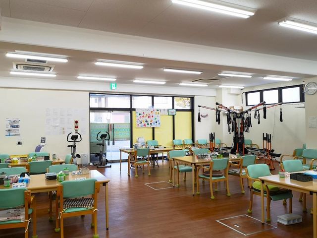 機能訓練室の明るい室内 機能訓練室 窓から光が入る、広めの機能訓練室です。運動機器や複数のテーブルが並び、作業しやすい環境が整っています。