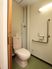 サムネイル 施設の写真 壁や便座の横にステンレス製の手すりが付いている。トイレのドアは引き戸である。トイレの上にトイレットペーパーが置かれている。