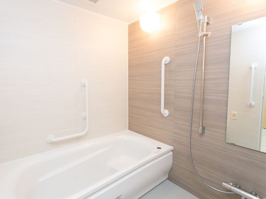 施設の写真 浴室内の様子。１人用の浴槽があり、手すりが設置されている。鏡の前の洗い場にシャワーチェアが置かれている。