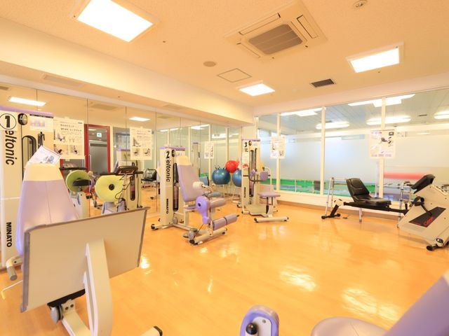 トレーニング器具が並ぶ部屋 マシーンルーム 光り輝く床と、整然と配置された最新のトレーニング器具が目を引く訓練スペースです。日々のリハビリや健康維持に最適な環境が整っています。