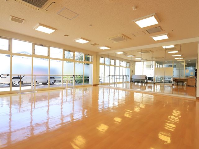 広々とした明るい空間 フィットネススタジオ 床が光沢を放つ広々とした空間で、体を動かしたりリハビリを行うことができます。大きな窓からは自然光が差し込み、明るい雰囲気を演出しています。