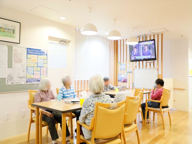 快適な居住スペース 共有スペース 明るく穏やかな午後のひととき、住居者が集まりテレビを観ながら過ごしています。様々な情報が掲示された壁は、日々のコミュニケーションに役立っている様子です。