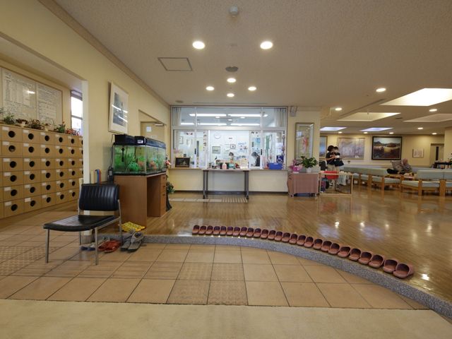 広々とした明るいロビー 玄関 清潔感のある広い空間には大小さまざまな椅子が配置されています。スタッフが対応するフロントも見え、明るく落ち着いた雰囲気です。
