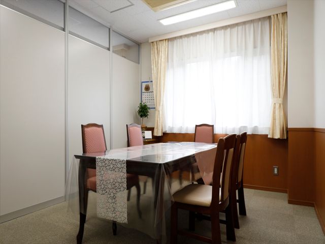 会議室のテーブルと椅子 談話室 落ち着いた色合いの多目的室には、丸みを帯びたテーブルが設置されており、複数の方が集まって対話を楽しむことができます。大きな窓から自然光が差し込み、明るい雰囲気を創出しています。