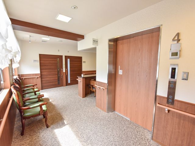 明るく広々とした廊下 エレベーターホール 落ち着いた色合いの広々とした通路で、訪問者を心地よく迎えます。待合椅子も配され、ゆったりとした時間を過ごせる空間です。