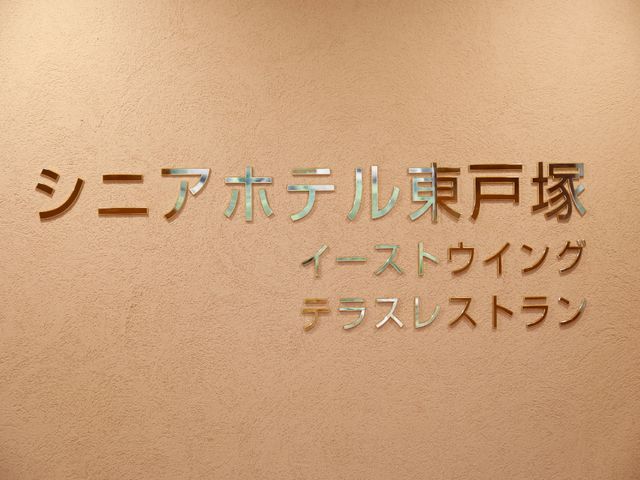 壁に掲示された金色文字 外観 清潔感のある壁に、品の良い金色の文字が印象的です。明るい未来への一歩を踏み出しませんか。