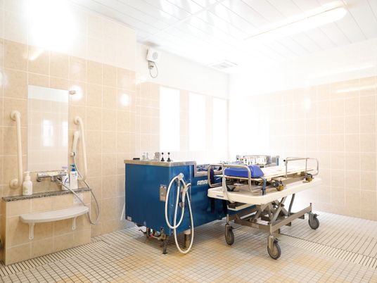 白色とベージュ色仕様の壁に側面が青色の機械浴が設置してある。浴槽の傍にはストレッチャーが置いてある。