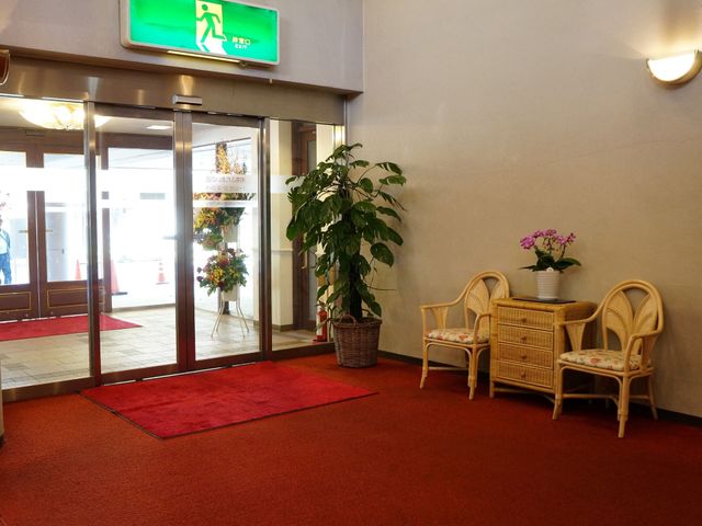 エントランスの植物と椅子 玄関 ゆったりとした空間のエントランスには、植物が飾られ落ち着いた雰囲気を醸し出しています。来訪者を温かく迎える配慮が見受けられます。
