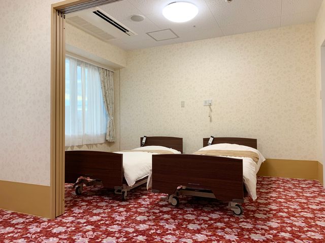 清潔な居室の模様 居室 ゆとりを持った居室には二つのベッドが配置され、過ごしやすい明るい雰囲気が漂います。窓からの自然光が柔らかく室内を照らしており、落ち着いた空間です。