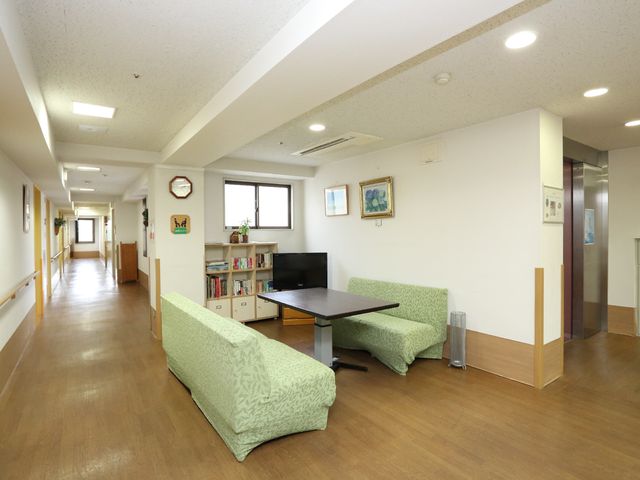 明るく広々とした共有スペース 談話スペース 広々としたラウンジは、日中の憩いの場としてゆとりをもってご利用いただけます。壁には時計や絵画が飾られ、くつろぎの時間を演出しています。
