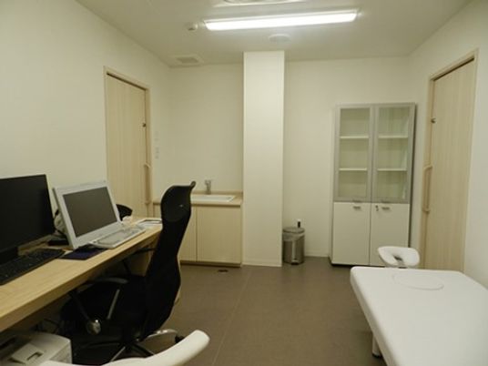 施設の写真 出入り口が2か所あり、手洗い場が取り付けられている。壁に向いてベッドやパソコンの置いてあるテーブルが置かれている。