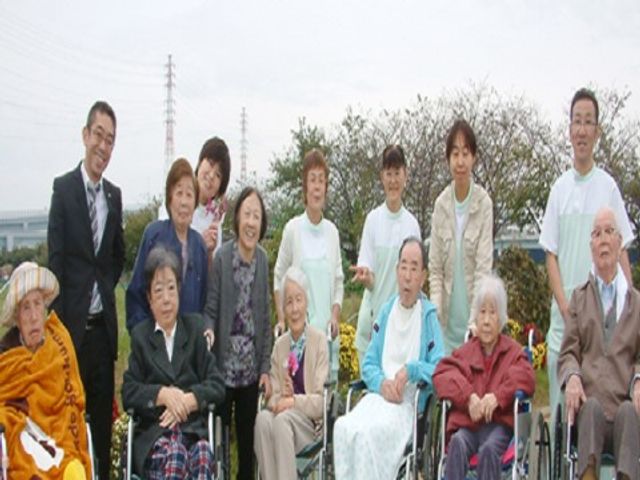 中庭での集合写真 外出イベント 心温まる中庭で、スタッフと利用者様が共に過ごす様子をご覧いただけます。明るい笑顔が印象的な瞬間です。