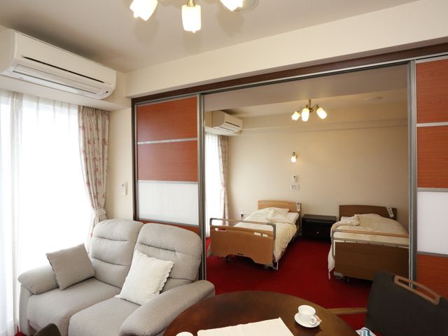 居心地の良い居室 2人用居室 広々とした居室は、暖かみのあるインテリアで、快適な日々を過ごせる設計です。ゆったりとしたソファや個別のベッドが配され、家庭のような雰囲気を大切にしています。