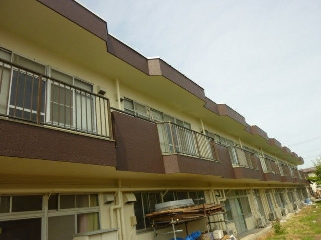 施設の外観 外観   横に長い建物で、各部屋の前に手すり付きのバルコニーが並んでいます。明るい空の下で、落ち着いた色合いの外まわりです。