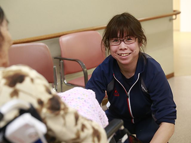 温かな交流の廊下 廊下 笑顔のスタッフが、車椅子を利用する入居者と親しげに会話しています。温かい雰囲気が漂います。