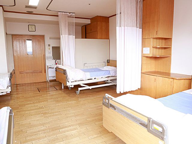ベッドとカーテンの居室 居室   広々とした居室には、自然光が差し込み、リラックスできる空間になっています。