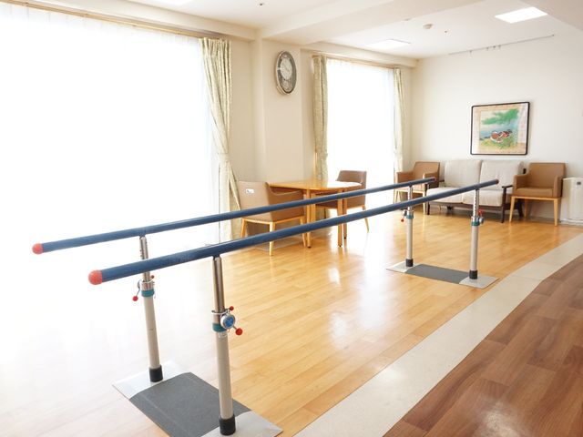 機能訓練室のバー訓練風景 共有スペース 明るい機能訓練室で、歩行支援のためのバーを備え、安全に体を動かせる環境が整っています。