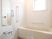 浴室は、全体的に白でまとめられたデザインになっている。窓から明るい光が差し込んでいる。壁には大きな鏡や手すりがある。