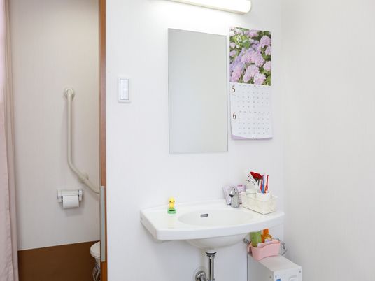 洗面スペースは、全体的に白でまとめられたデザインである。壁には大きな鏡が付いていて、すぐ横にカレンダーが貼ってある。
