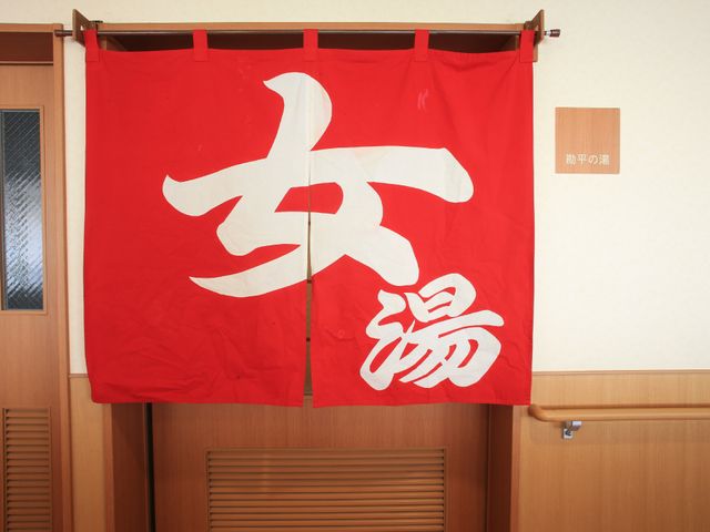 赤い暖簾と掲示物 大浴場 和気藹々とした雰囲気の中で、お一人おひとりの暮らしを支えるここでの仕事は、多くのやりがいを感じることでしょう。