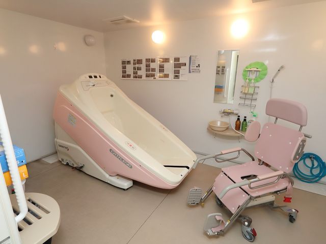 ケア用バスタブとシャワーチェア 機械浴室 ゆったりとしたバスタブと調整可能なシャワーチェアが備わった清潔な浴室です。利用者の快適な入浴をサポートする環境が整っています。