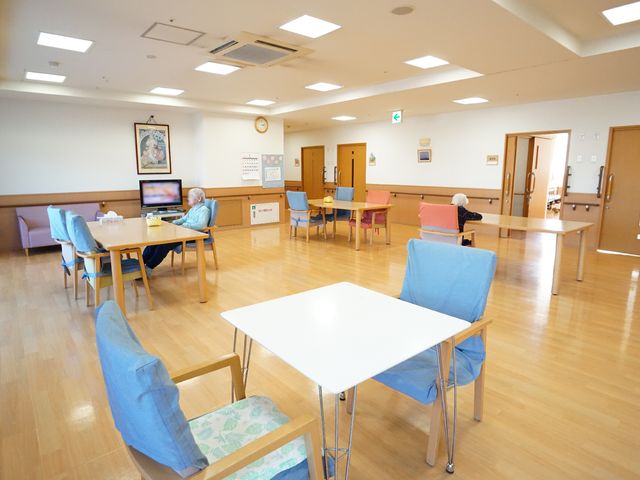 広々とした明るい施設の食堂 共有スペース ゆったりとした空間でテレビを観ることができ、窓からの自然光が心地よい食堂です。利用者の方々がそれぞれの時間を過ごされています。